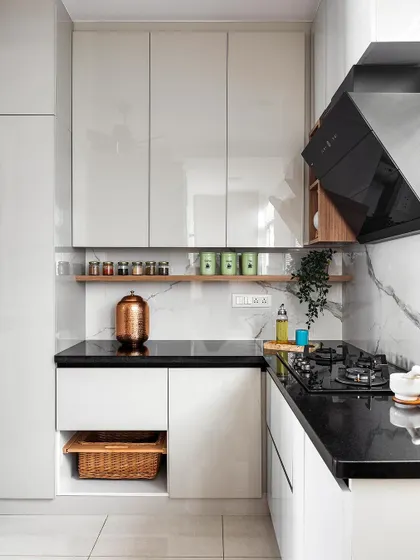 A view of the cooking zone in this modern kitchen. It includes an open wooden shelf for easy access to spices, handleless cabinets for a sleek finish, and a wicker basket integrated into the base unit for storing vegetables.