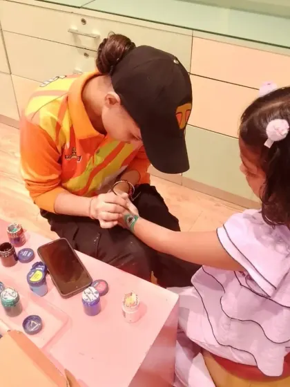 A staff member paints a beautiful design on a child's arm. We offer this as a fun activity for birthday parties or special events like Janmashtami.