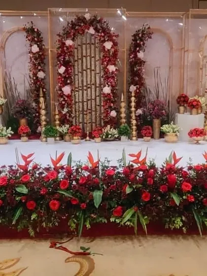 This engagement stage features a sophisticated design with gold-finished metallic arches and panels. The decor is completed with rich red and white floral arrangements.
