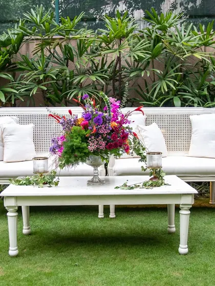 A close-up of the white lounge furniture, featuring a stunning centerpiece of colorful, jewel-toned flowers. The vibrant arrangement provides a beautiful contrast to the neutral furniture.