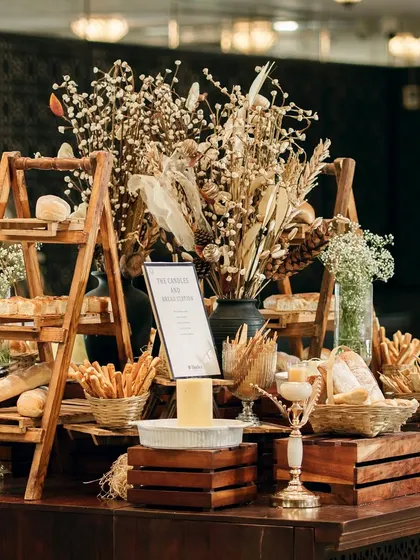 A rustic bread and cheese station, complete with a variety of artisanal loaves, breadsticks, and a warm cheese fondue. The wooden crates and dried flowers add to the charming, rustic aesthetic.