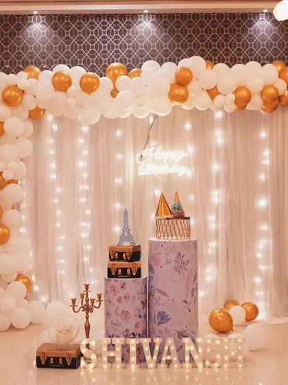 A beautiful and simple decor for Shivansh's first birthday. The white and gold balloon arch against a fairy light curtain backdrop is both elegant and celebratory.