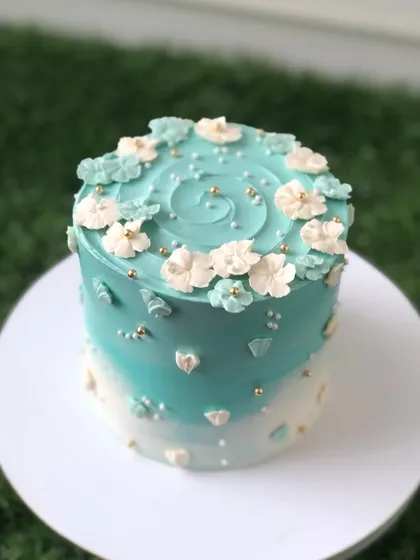 A beautiful teal ombre cake with a swirl top and delicate white and teal flowers.