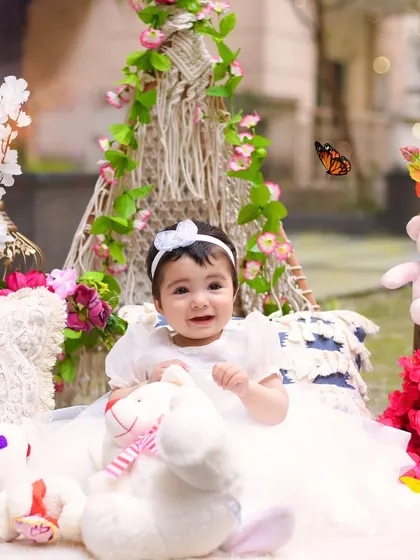 This little girl in a white dress looks angelic in our outdoor floral teepee setup, surrounded by soft pillows and teddy bears.