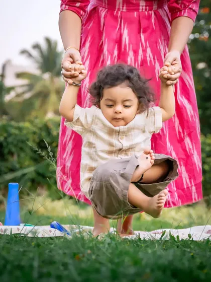 Taking those wobbly first steps with mom's helping hands. This adorable action shot captures a baby's determination and a mother's gentle support during an outdoor play session on the grass. It’s these fleeting stages of growth that I love to preserve.
