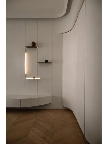 The smooth curves of the master bedroom wardrobe create a gentle, flowing line. This detail, combined with the herringbone wood flooring, adds a layer of refined craftsmanship to the minimalist design.