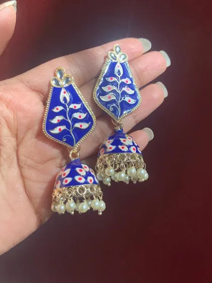 A stunning pair of royal blue Meenakari jhumkas with a leaf-like motif hand-painted in white and red. The pearl drops add a classic finishing touch.