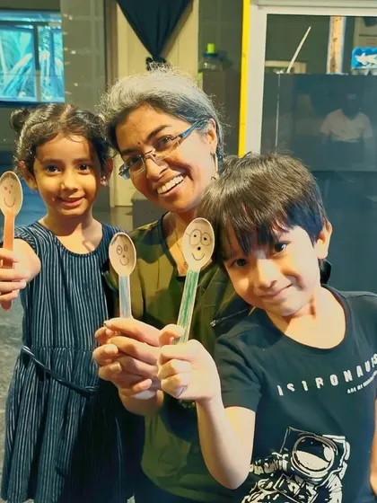 Fun with spoon puppets! A facilitator and two young students proudly display the simple yet expressive puppets they created in a workshop. Creativity can be found in the simplest of objects.