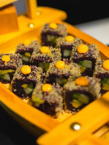 Creative purple rice sushi rolls presented in a wooden boat.