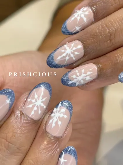 Jingle all the way with these winter wonderland nails. This design features a glittery blue French tip on natural-length nails, decorated with hand-painted white snowflakes.