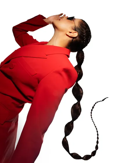 A high-fashion shot with a bold red suit and a creative, sculptural hairstyle. The high-key lighting and dynamic pose create a striking image.