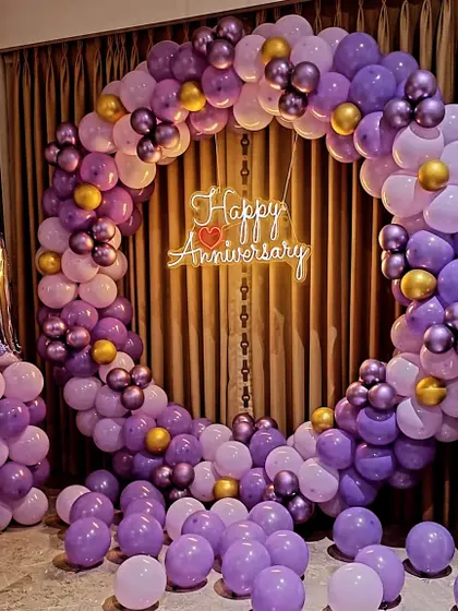 A first-anniversary decoration with a full ring of purple and gold balloons and a neon sign.
