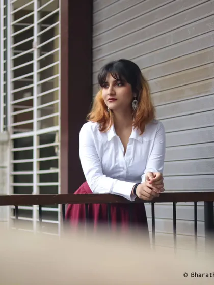 A thoughtful, looking-away pose on an urban balcony. The clean lines of the building create a minimalist backdrop.