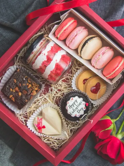 A Valentine's Day hamper filled with treats made with love. It includes a red velvet jar, assorted macarons, brownies, and a custom cupcake.