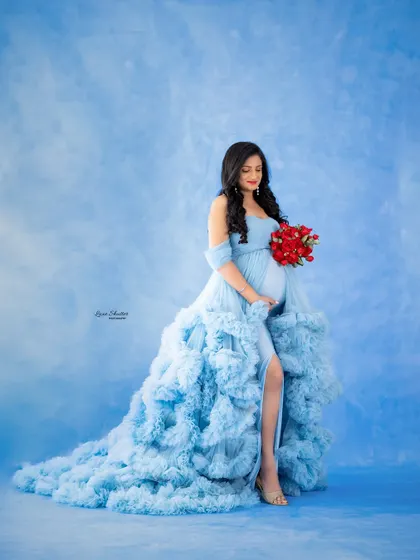 A pop of color with a bouquet of red roses contrasts beautifully with the soft blue ruffled gown and matching backdrop.