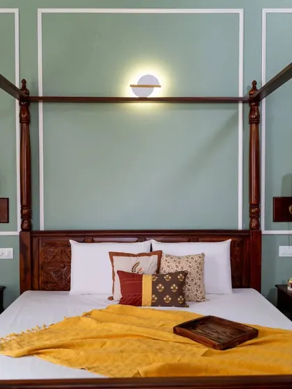 A straight-on view of the four-poster bed, with its beautifully carved headboard and a backdrop of a gentle green wainscoted wall.