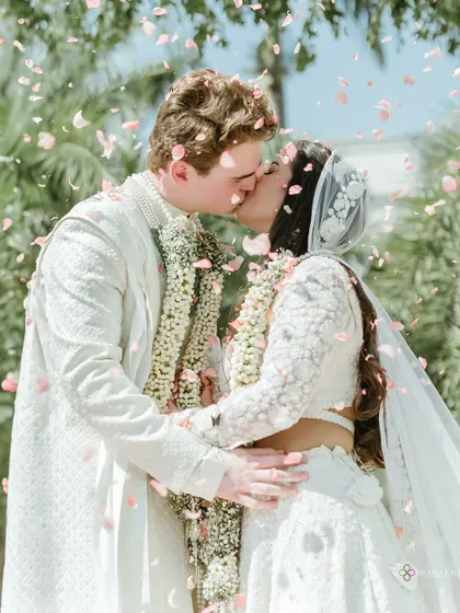 An intimate kiss under a shower of petals, a perfect fairytale ending to a beautiful cross-cultural wedding ceremony.