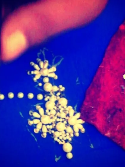 A macro view of delicate pearl embroidery in progress. Each pearl is carefully stitched by hand to form intricate floral patterns, adding a touch of timeless elegance to the garment.
