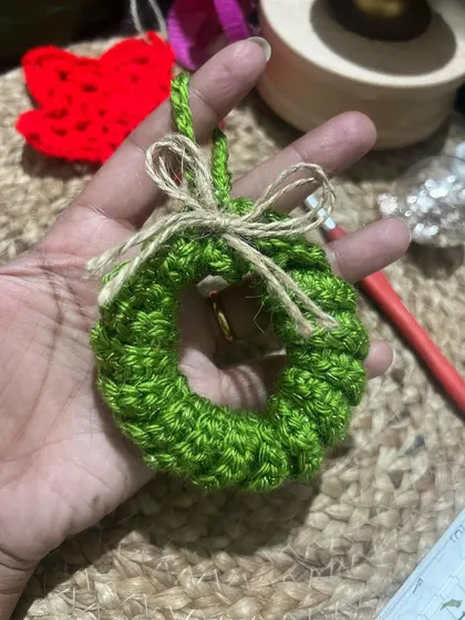A handmade mini Christmas wreath ornament, held in my hand to show its cute size. It's perfect for decorating the tree or even as a unique gift tag.