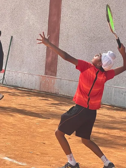 A young player with a turban practicing his serve, showing the explosive upward motion we teach. Our academy welcomes players from all backgrounds.