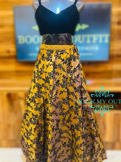 This party wear lehenga features a yellow skirt with black floral flocking and a simple black velvet blouse. It's a bold and modern choice for an evening event.