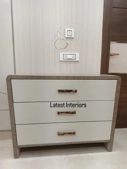 A detail shot of a custom-made side table with a wood-grain frame and high-gloss white drawers. The unique rose gold handles add a touch of bespoke luxury.