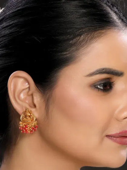 This image showcases a temple-inspired earring with intricate carvings and red beadwork, ideal for a cultural jewellery brand.