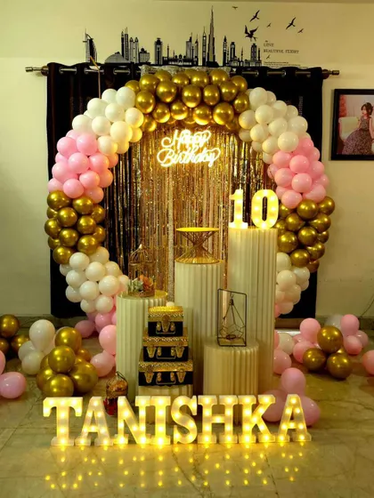 A 10th birthday party with a circular balloon arch in pink, white, and gold. The decor features a shimmer curtain, plinths, and marquee letters and numbers.