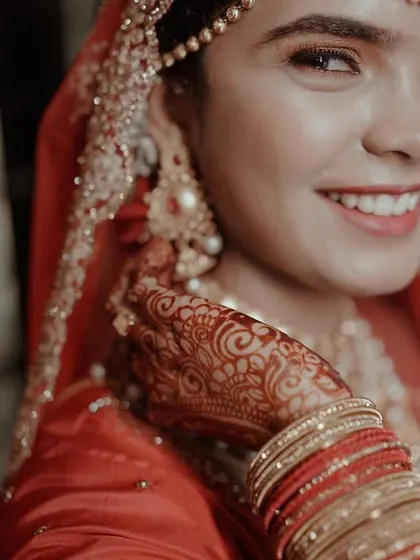 A close-up portrait of a beautiful bride in her red wedding attire, her happy smile and intricate henna making for a perfect shot.