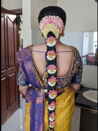 A vibrant bridal look with a traditional braid decorated with pink and white flowers and matching 'Jada Billa' ornaments.