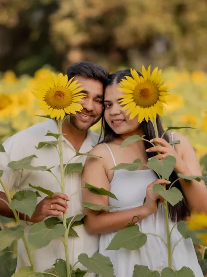 A fun and creative pre-wedding photo of the couple peeking out from behind sunflowers, showcasing their happy and carefree connection.