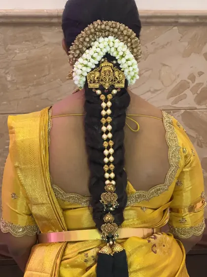 A traditional bridal braid that tells a story of love and culture. This style features a long, thick braid decorated with pearl-studded ornaments and finished with a classic kunjalam.