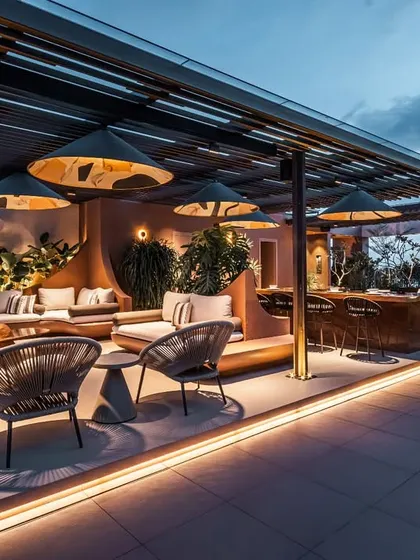 A wide evening shot capturing the full ambiance of the illuminated terrace. The lighting design accentuates the architectural forms and lush plantings, creating a dramatic and magical nighttime environment.