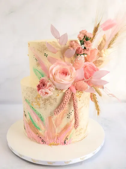 This boho-chic wedding cake features hand-painted pastel strokes and delicate gold speckles. The look is finished with an arrangement of dried wheat, pampas grass, and soft pink sugar flowers.