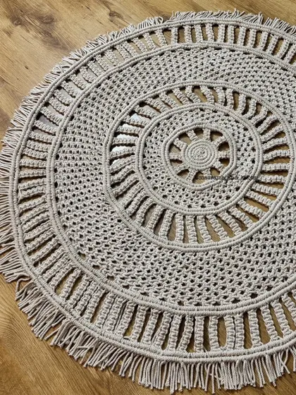 A close-up of the macrame rug, showing the detailed knot work and the sun-like pattern in the center.