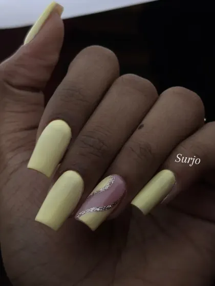 A cheerful and bright set featuring matte yellow square nails with a single accent nail that has a diagonal splash of silver glitter over a sheer base.