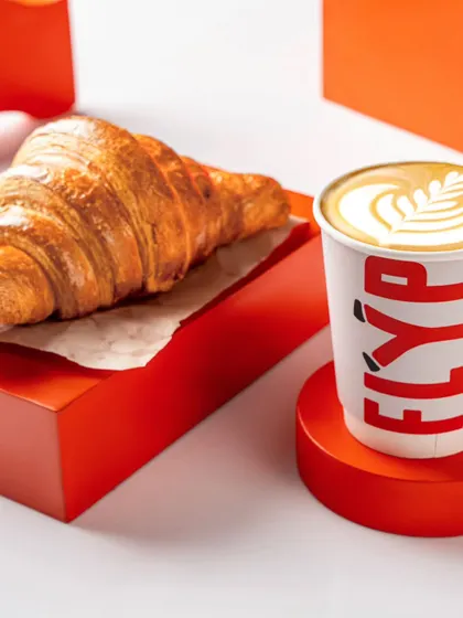 A close-up of a Flyp Coffee cup next to a flaky croissant. The focus on texture and the clean, minimalist setup makes the pairing look irresistible.