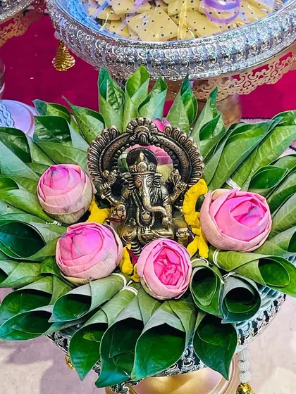 A beautiful aarathi plate with a Ganesha idol placed on a bed of betel leaves and decorated with pink lotus buds. This is a perfect centerpiece for any puja or traditional ceremony.
