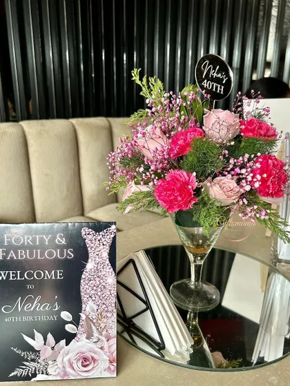 A tabletop decor detail from the 40th birthday party. The custom "Forty & Fabulous" welcome card and a vibrant floral centerpiece in a cocktail glass add a touch of elegance to the guest seating areas.