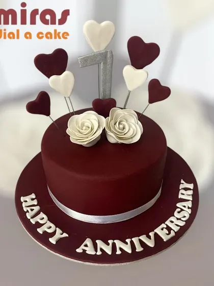 A rich and romantic first-anniversary cake. The deep red fondant is decorated with white and red hearts and two white roses, symbolizing a year of love.