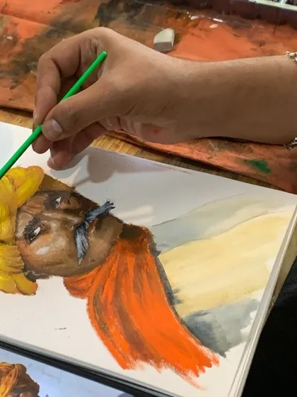 A student works on a watercolor portrait, carefully layering washes to build skin tones and capture expression. This image shows the focus and technique involved in our professional painting classes.