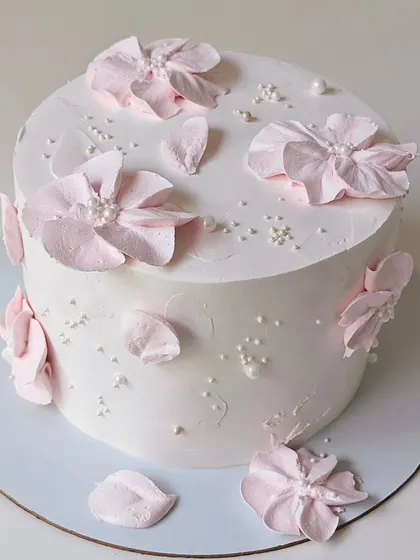 An elegant white cake featuring delicate, hand-sculpted pink wafer paper flowers. The scattered pearls add a touch of sophistication to this minimalist design.