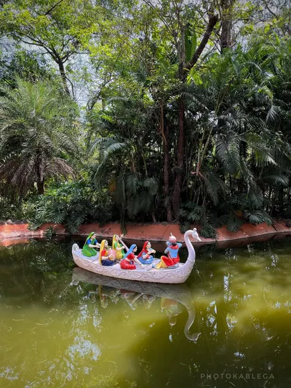 A serene scene of deities in a swan-shaped boat on a small pond within the ecovillage.
