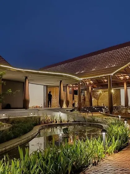 As dusk falls, the architectural lighting at the Madurai resort highlights its curving forms and rich textures. The design creates a warm and inviting ambiance, with pathways and water features gently illuminated.