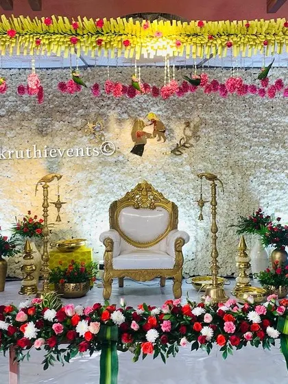 An elegant all-white backdrop made of dense jasmine flowers. The stage is framed by traditional flower pillars and accented with red roses, creating a look of pure sophistication.