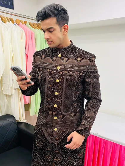 A candid shot of a client checking his phone while wearing the luxurious brown and gold embroidered bandhgala.