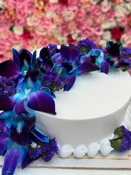 An elegant white cake decorated with beautiful fresh blue orchids. Using fresh flowers is a great way to add a natural and sophisticated touch.