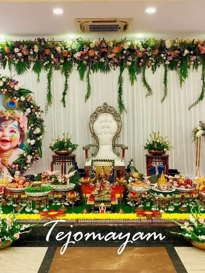 A beautiful baby shower setup with a custom backdrop with a mother and child portrait, surrounded by floral arrangements and a full display of traditional plates.