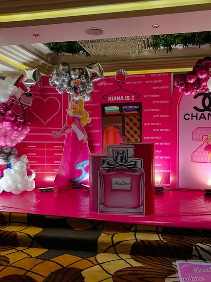 A full view of the pink fashion-themed birthday stage, complete with balloon garlands, a personalized backdrop, and large, fun props.