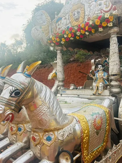 A silver-colored chariot with two horses, decorated with a simple floral arrangement on top for a procession.